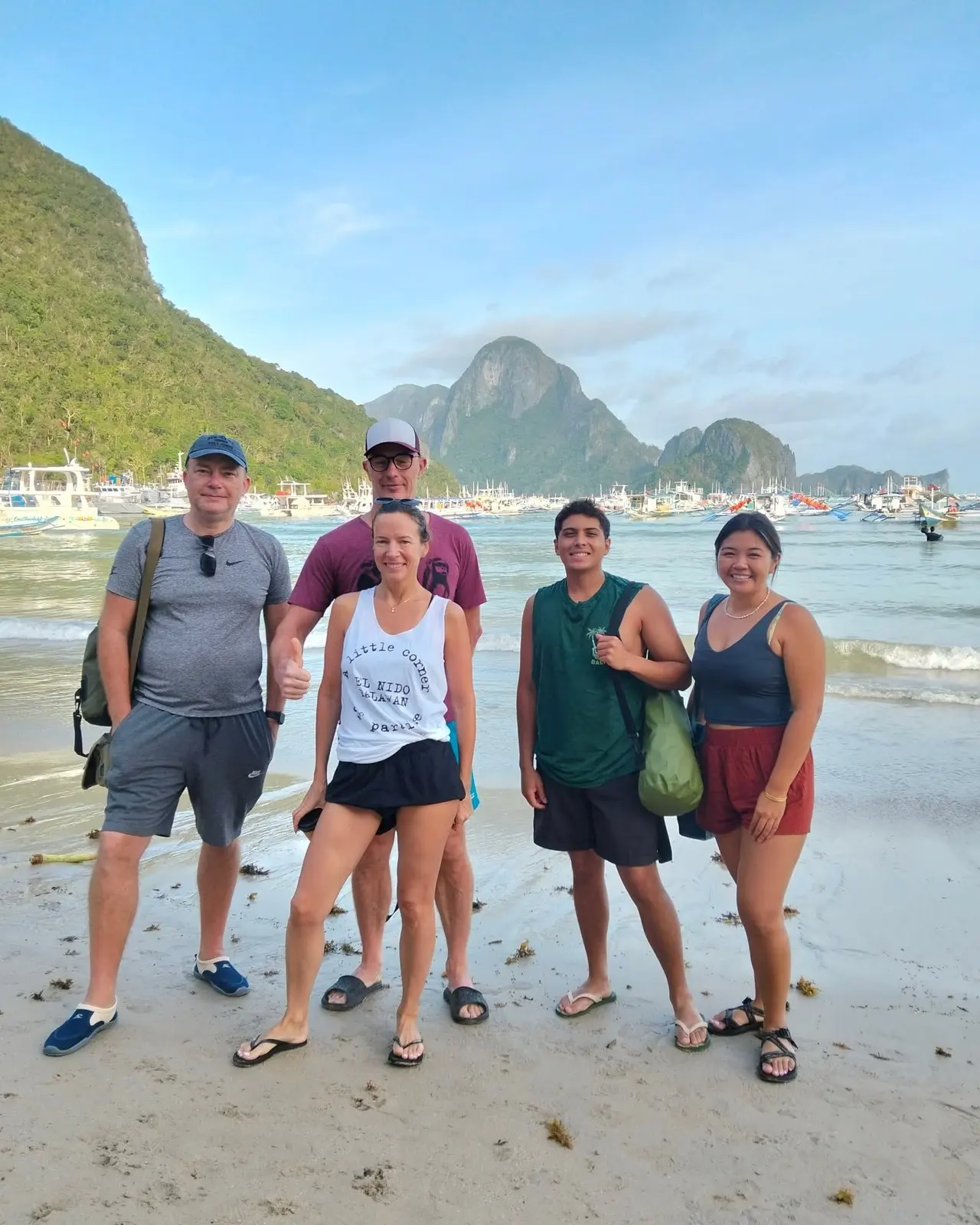 Four friends on a quiet beach with boats and hills behind