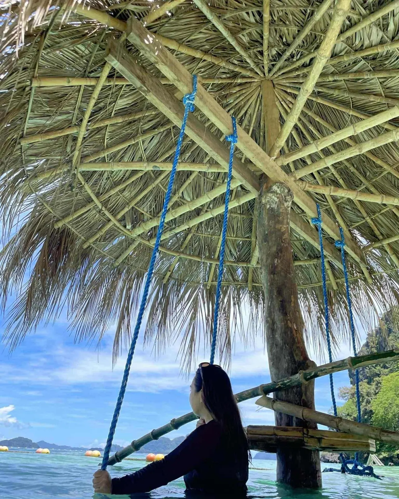A guest on a rope swing under a thatched roof, facing the sea
