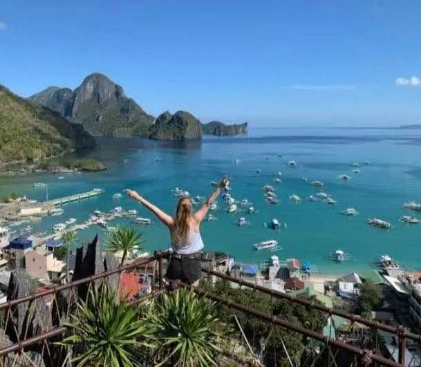 Arms wide at a viewpoint over El Nido bay and its boats